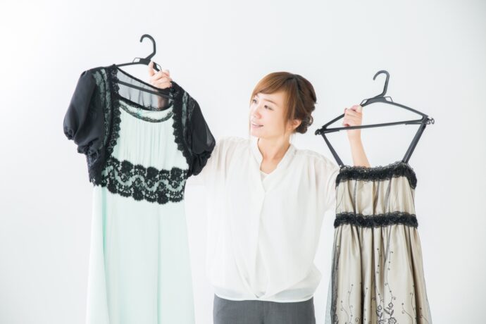 画像：両手に白いドレスを持って悩む女性