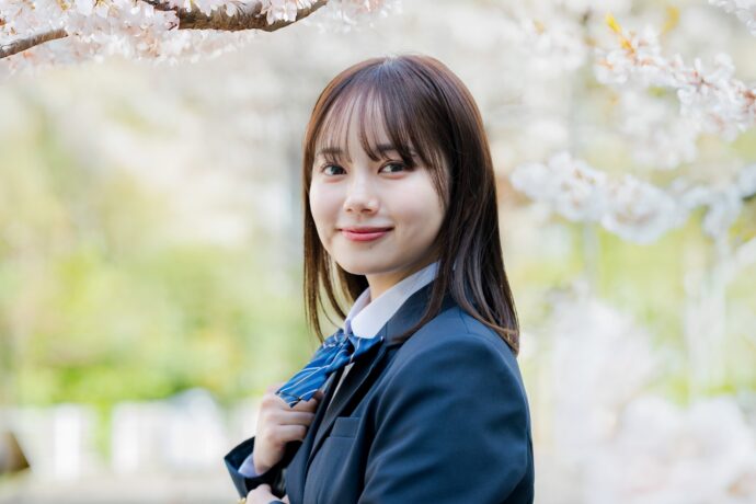 画像：桜の前で振り向く制服姿の女子生徒