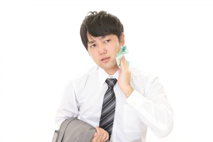 画像：汗を拭くスーツの男性