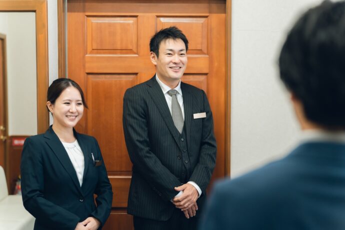 画像：客人を迎えるスーツの男女