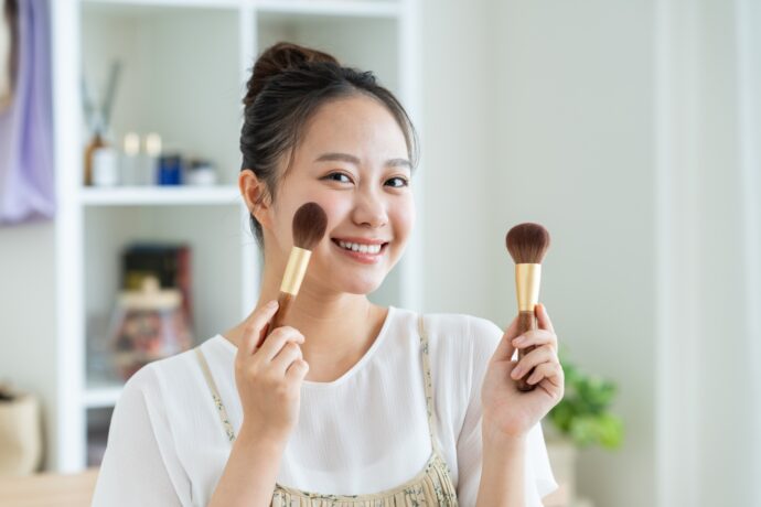 画像：メイクブラシを顔に当てる笑顔の女性