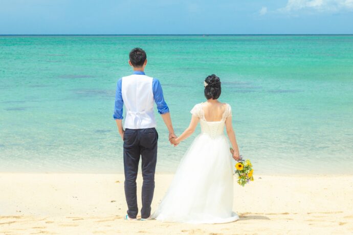 画像：海をバックに手を繋ぐ新郎新婦