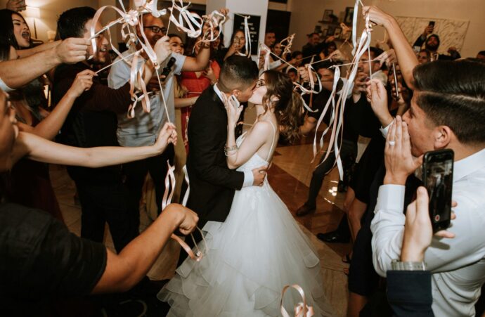 画像：ゲストにリボンワンズで祝われる中キスをする新郎新婦