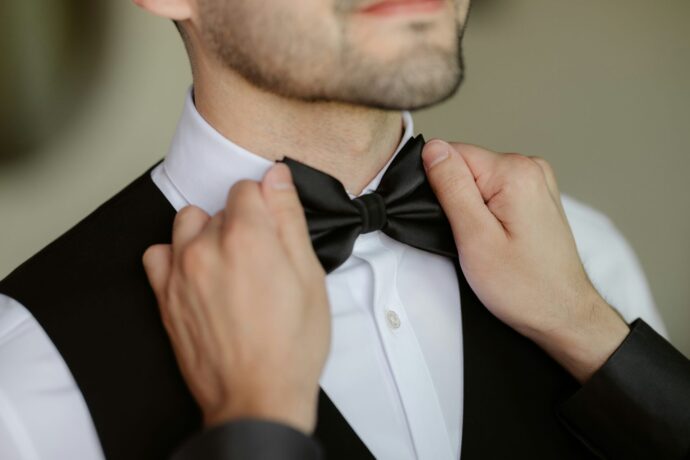 画像：黒い蝶ネクタイを締めてもらう男性