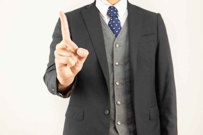 画像：人差し指を立てるスーツの男性