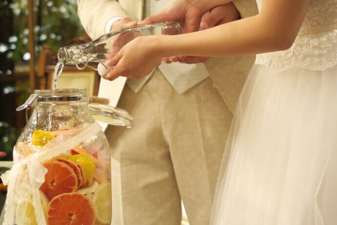 画像：フルーツの入ったガラス瓶にリキュールを注ぐ新郎新婦