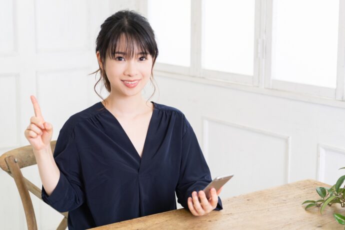 画像:スマホを片手に人差し指を立てる女性