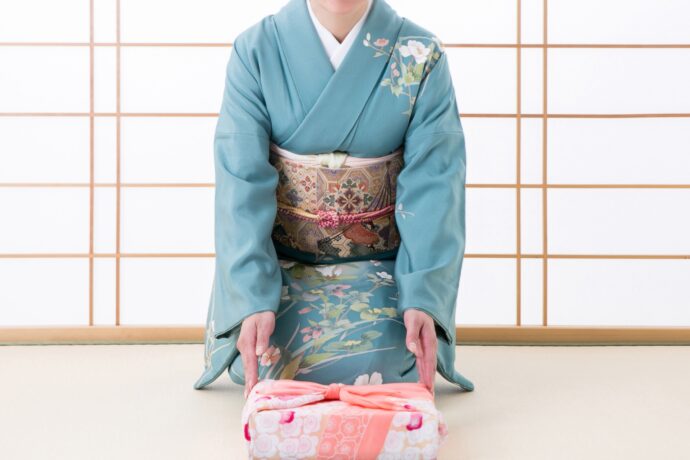 画像：風呂敷に包まれた箱を差し出す着物の女性