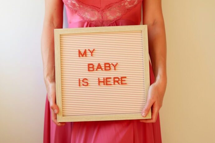 画像：MY BABY IS HERE と書かれたプレートを持った女性